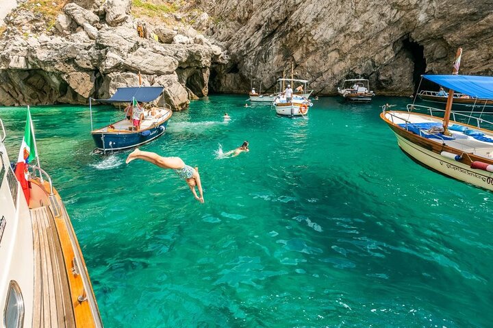 Bagnanti si tuffano da una barca nell'acqua verde e limpida vicino alle grotte marine di Capri