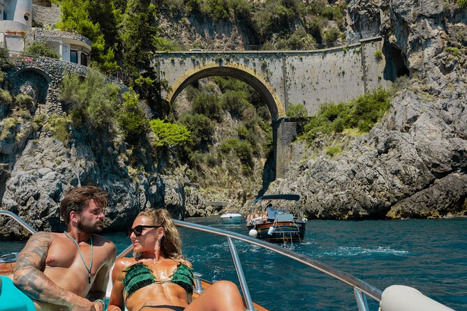 Couple relaxing on a boat below the arched bridge of the Fiordo di Furore